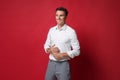 Smiling young business man in white shirt, gray pants posing isolated on bright red wall background studio portrait Royalty Free Stock Photo