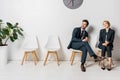 smiling young business people holding paper cups and looking away while waiting on chairs Royalty Free Stock Photo