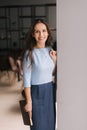 Smiling young business woman holding file folder while standing near window in modern office room. Royalty Free Stock Photo