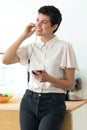 Smiling young business woman using her free hands to make a call with mobile phone while standing in the office Royalty Free Stock Photo