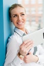 Smiling young business woman using tablet PC while standing relaxed near window at her office Royalty Free Stock Photo