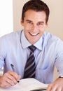 Making sure his dayplanner is filled out. Smiling young businessman filling in his dayplanner.