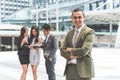 Smiling young businessman looking into camera with his arms crossed and teammates background in urban. Modern business office team Royalty Free Stock Photo