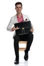 Smiling young businessman sitting and presenting his briefcase Royalty Free Stock Photo