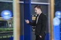 Smiling young businessman standing in front of an ATM and looking at his phone Royalty Free Stock Photo