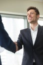 Smiling young businessman wearing black suit shaking male hand, Royalty Free Stock Photo