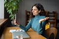 Smiling young businesswoman in earbuds sitting at office desk talking by video call on smartphone Royalty Free Stock Photo