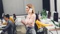 Smiling young businesswoman holding cup and talking by smartphone while colleagues working behind Royalty Free Stock Photo