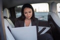 Smiling young businesswoman looking at laptop screen while sitting on the back seat of car, working online. Business Royalty Free Stock Photo