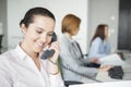 Smiling young businesswoman using landline telephone with colleagues in background at office