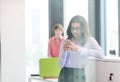 Smiling young businesswoman using mobile phone with male colleague in background at office Royalty Free Stock Photo