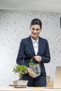 Smiling young businesswoman watering plant on desk against brick wall at office Royalty Free Stock Photo