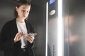 Smiling young businesswoman is writing messages on her mobile phone in the lift. Female office worker is texting messages on the Royalty Free Stock Photo