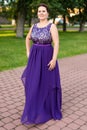 Smiling young Caucasian brunette woman in purple floor-length dress with embroidery in park Royalty Free Stock Photo