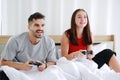 Smiling young Caucasian lover Couple hand holding joysticks and playing game play station together in bedroom. Lifestyle and Royalty Free Stock Photo