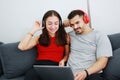 Smiling young Caucasian lover Couple listening to online music with Headphones and laptop together in living room. Royalty Free Stock Photo