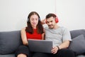 Smiling young Caucasian lover Couple relish for listening to online music with Headphones and laptop together in living room. Royalty Free Stock Photo