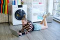 Smiling young Caucasian woman relaxing with laptop for comunucation media while waiting for the washing machine to finish cleaning