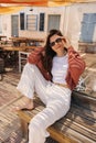 Smiling young caucasian woman sitting on bench outside summer cafe near beach. Royalty Free Stock Photo