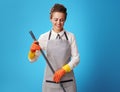 Smiling young cleaning lady in apron on blue using mop