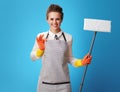 Smiling young cleaning lady in apron with mop on blue