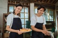 smiling young couple of cake makers wearing aprons holding up a tray of cooked cakes Royalty Free Stock Photo