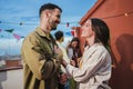 Smiling young couple flirting and having fun at a rooftop party with friends, drinking beer, enjoying and having a