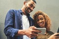 Smiling young couple looking, laughing and holding phone together showing a funny social media app. Friends sharing a