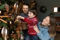 Smiling young couple parents decorating tree with kid. Royalty Free Stock Photo