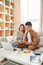 Smiling young couple sit on couch using laptop taking care of utility bills and house, read paperwork Royalty Free Stock Photo