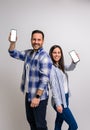 Smiling young couple standing back to back and showing blank screen of smart phones. Portrait of happy boyfriend and girlfriend