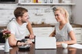 smiling young couple talking and looking at each other while using laptop together