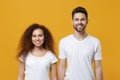 Smiling young couple two friends european guy african american girl in white t-shirts posing isolated on yellow wall Royalty Free Stock Photo