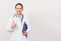 Smiling young doctor woman with stethoscope showing thumbs up isolated on white background. Female doctor in medical gown holding Royalty Free Stock Photo