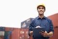 Smiling young engineer in protective work wear in a shipping yard examining cargo