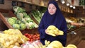 Smiling young european woman in traditional islamic dress and khimar successful owner of fruit and vegetable store