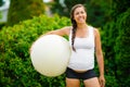 Smiling Young Expectant Mother Holding Exercise Ball In Park