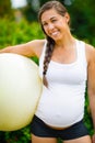 Smiling Young Expectant Mother Holding Fitness Ball In Park