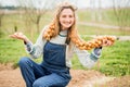 A smiling young farmer girl in a field in a denim overalls holds a bunch of onions. Planting bulbs in the ground in the