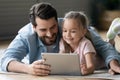 Smiling young father watching cartoons on tablet with small daughter.