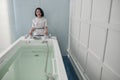 Smiling assistant prepares hydro massage bath full of clear water in spa salon Royalty Free Stock Photo