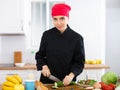 Smiling female chef in black uniform preparing vegetable salad in private kitchen Royalty Free Stock Photo