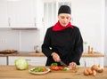 Smiling female chef in black uniform preparing vegetable salad in private kitchen Royalty Free Stock Photo