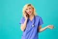 Smiling young female doctor or nurse wearing blue scrub uniform and stethoscope talking on mobile phone Royalty Free Stock Photo