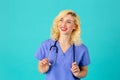 Smiling young female doctor or nurse wearing blue scrubs and stethoscope looking up Royalty Free Stock Photo