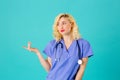 Smiling young female doctor or nurse wearing blue scrubs and stethoscope, pointing and looking to side Royalty Free Stock Photo