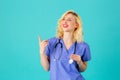 Smiling young female doctor or nurse wearing blue scrubs and stethoscope, pointing and looking to side Royalty Free Stock Photo