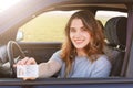 Smiling young female with pleasant appearance shows proudly her drivers license, sits in new car, being young inexperienced driver Royalty Free Stock Photo