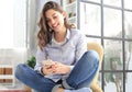 Smiling young female sitting in the armchair in the living room and using with her mobile phone Royalty Free Stock Photo