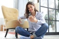 Smiling young female sitting on the floor in the living room and using with her mobile phone Royalty Free Stock Photo